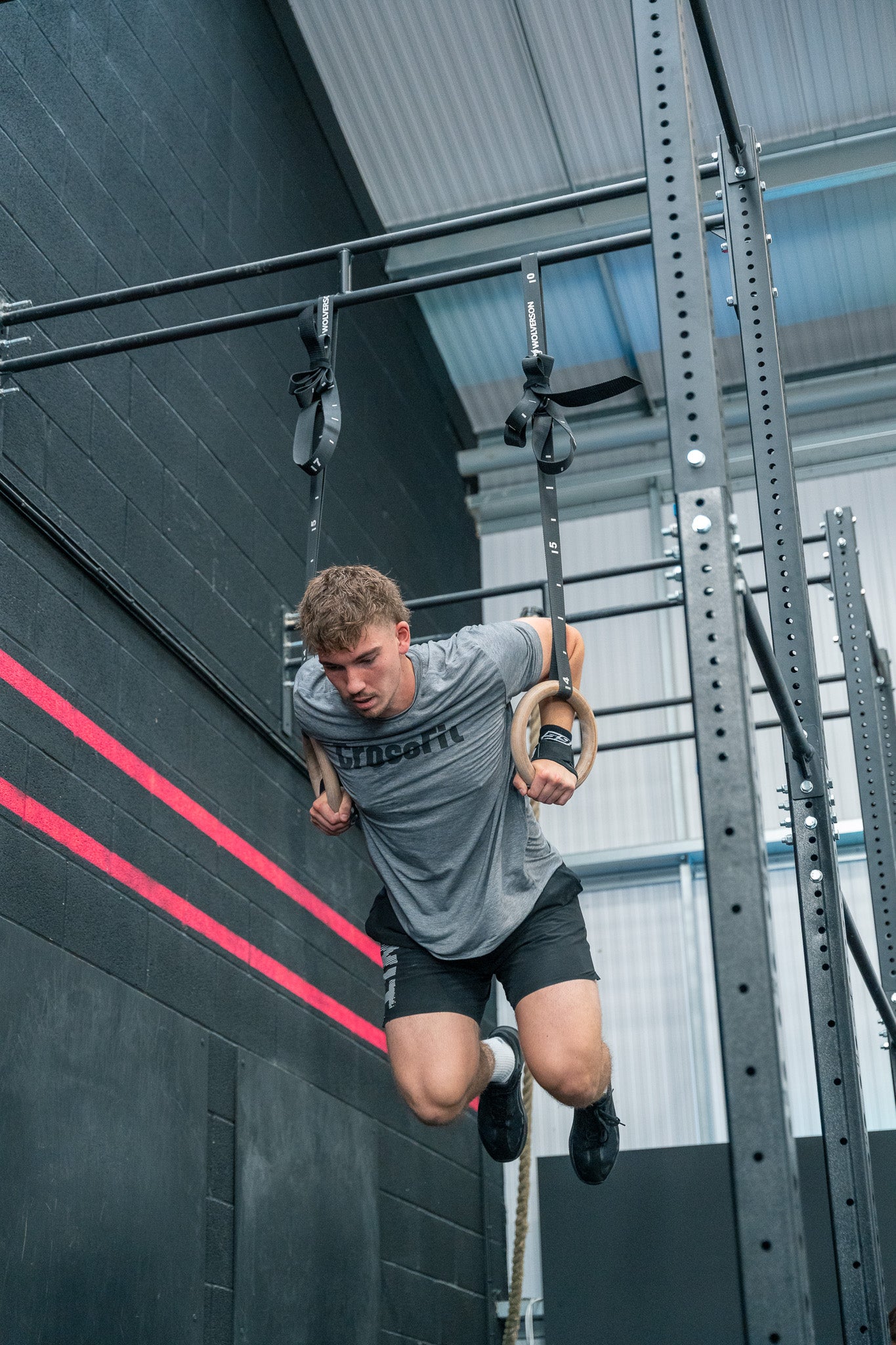 Illustration of a vivid CrossFit competition occurring in a large, energetic gymnasium. In the foreground, a Hispanic female athlete is doing box jumps with determination, while a Caucasian male compe